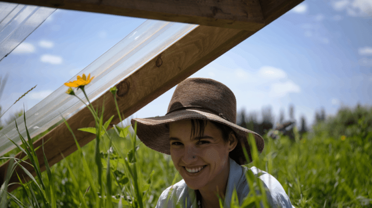 Person sitting in a field wearing a sun hat. A yellow flower is to the left of the person.