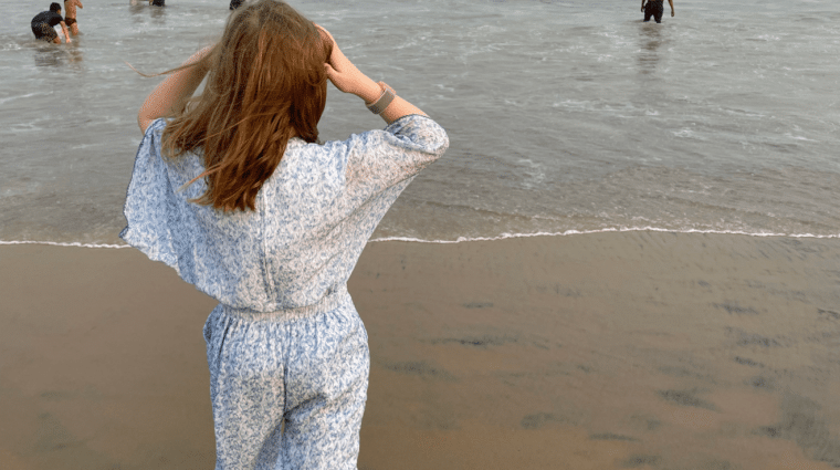 Photo is taken from behind a person standing on the shore looking towards water. There are people in the water.