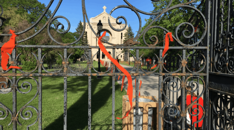 Orange ribbons on a wrought iron gate. Green grass and tall stone building in the background.
