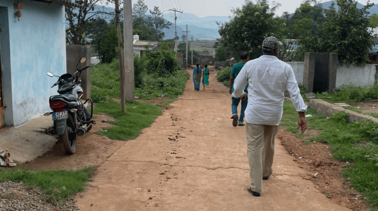 Photo is taken from behind people walking on a path. A motorcycle is parked to the left. Power lines are overhead.