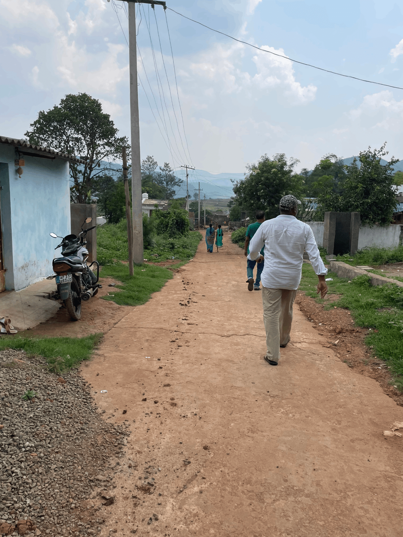 Photo is taken from behind people walking on a path. A motorcycle is parked to the left. Power lines are overhead.