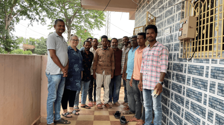 A group of 12 people standing next to a building looking towards the photographer.