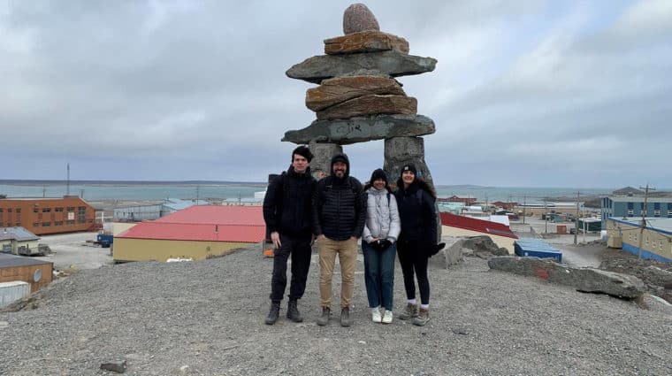 Photo of a group of people standing in front of a large Inukshuk in Rankin Inlet, Nunavut