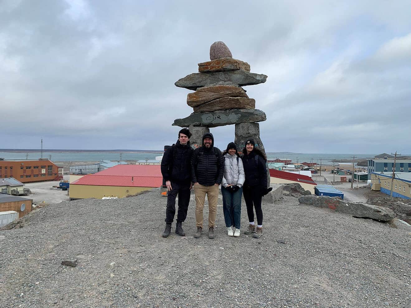 Photo of a group of people standing in front of a large Inukshuk in Rankin Inlet, Nunavut