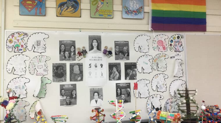 This is a picture of a classroom bulletin board that shows models of Deoxyribonucleic acid (DNA), and images of women scientists and Pride flag. 
