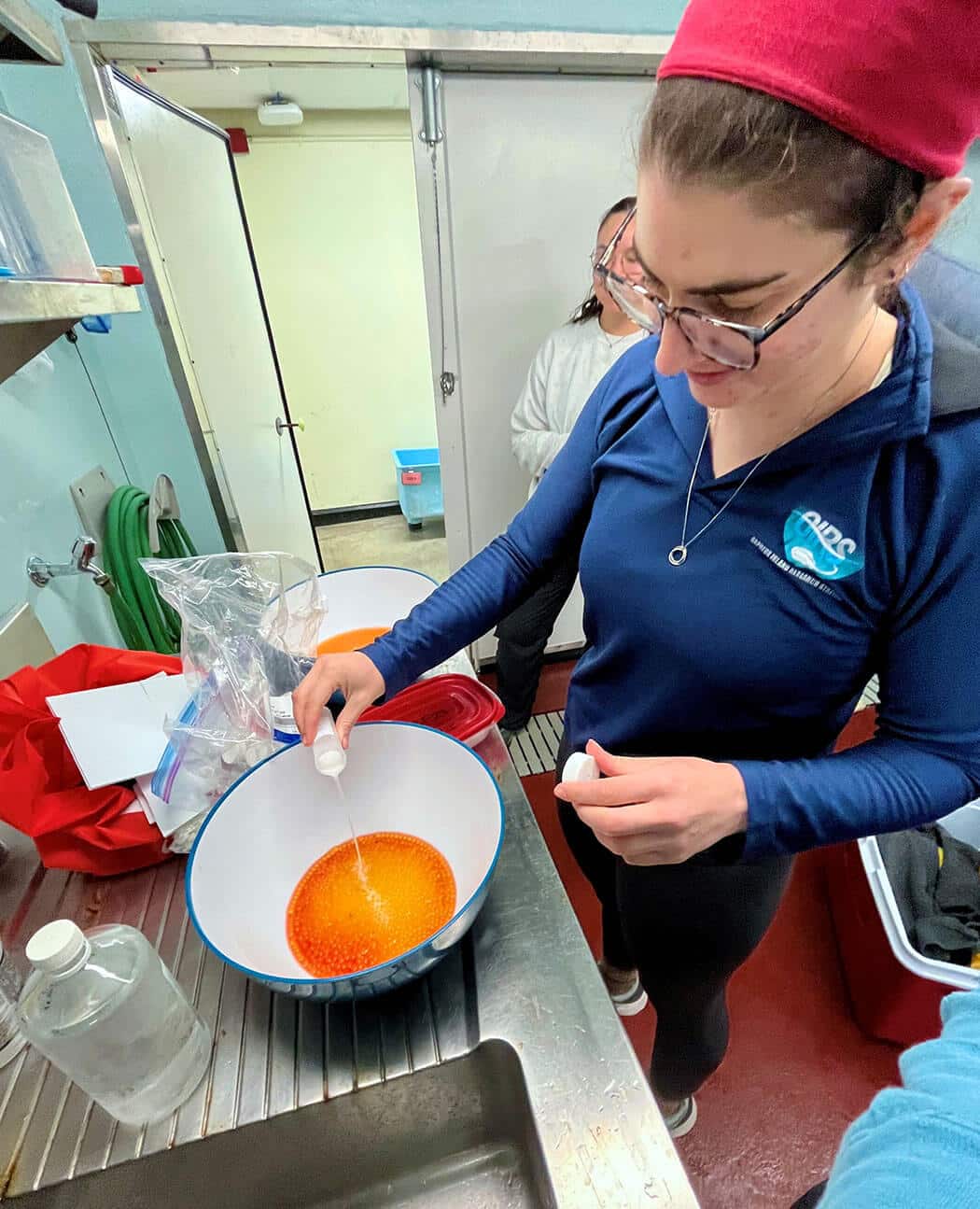 Researcher pouring liquid into a bowl of orange fish eggs.