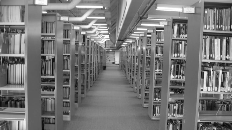 Black and white photo of the Library's 5th floor. Rows of book shelves on the right and left sides. The centre is an open path.