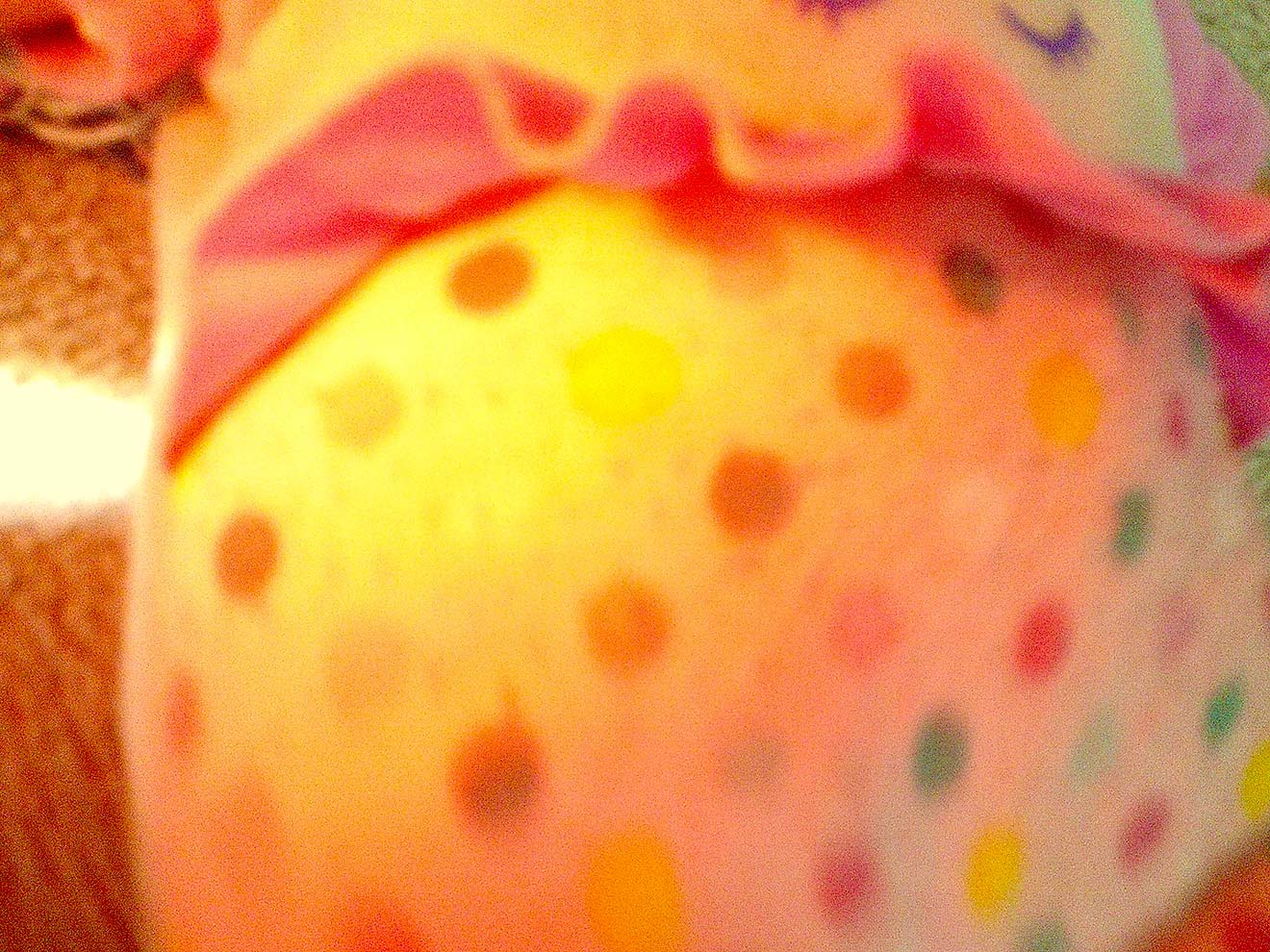 A pink, yellow, and turquoise doll abdomen is featured as an abstract close up. The head and legs of the doll are off-camera.