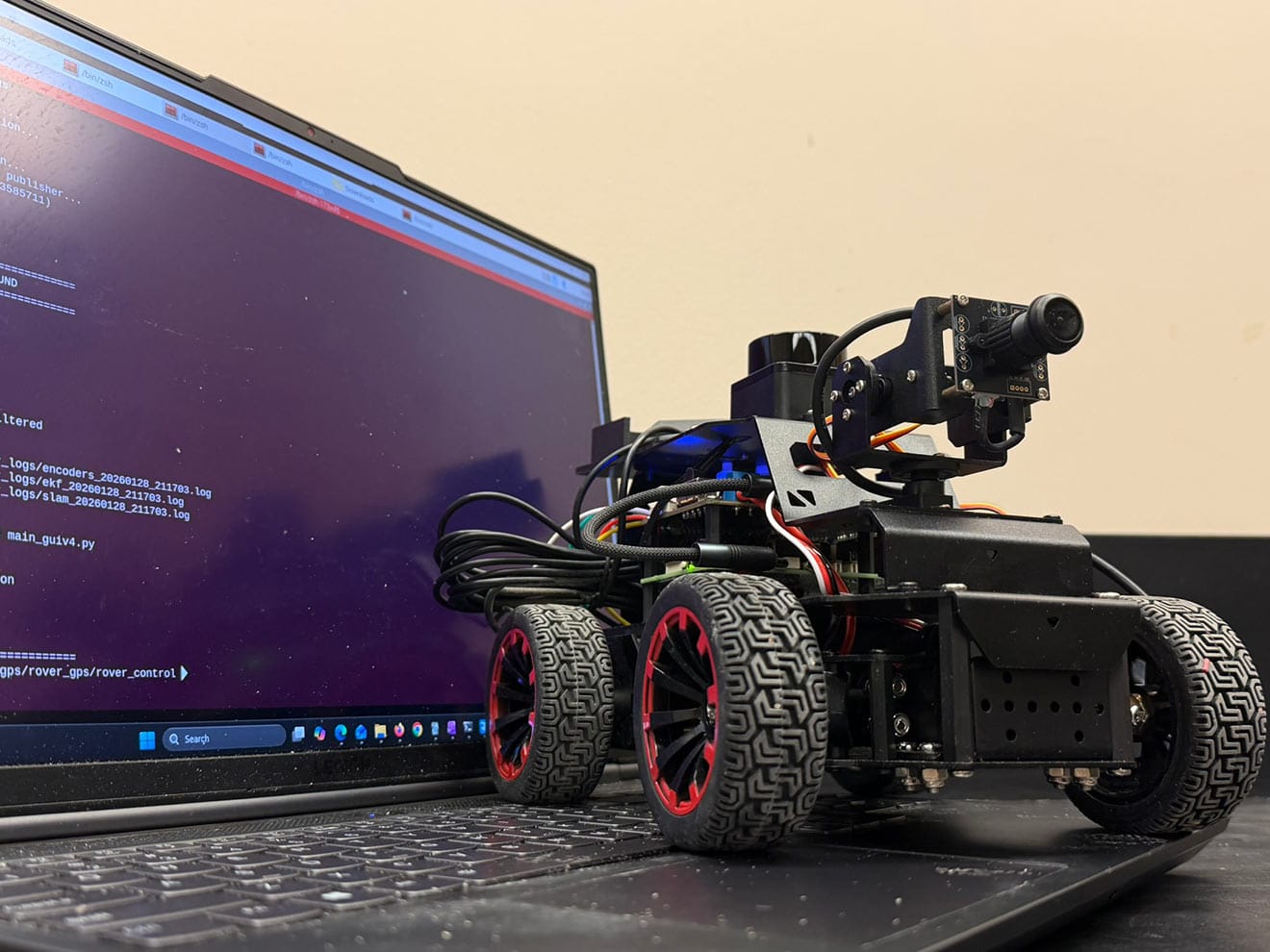 Autonomous rover with sensors and camera next to laptop in research lab setting